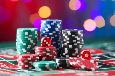 Photo of Casino chips and dice on roulette table against blurred lights, closeup