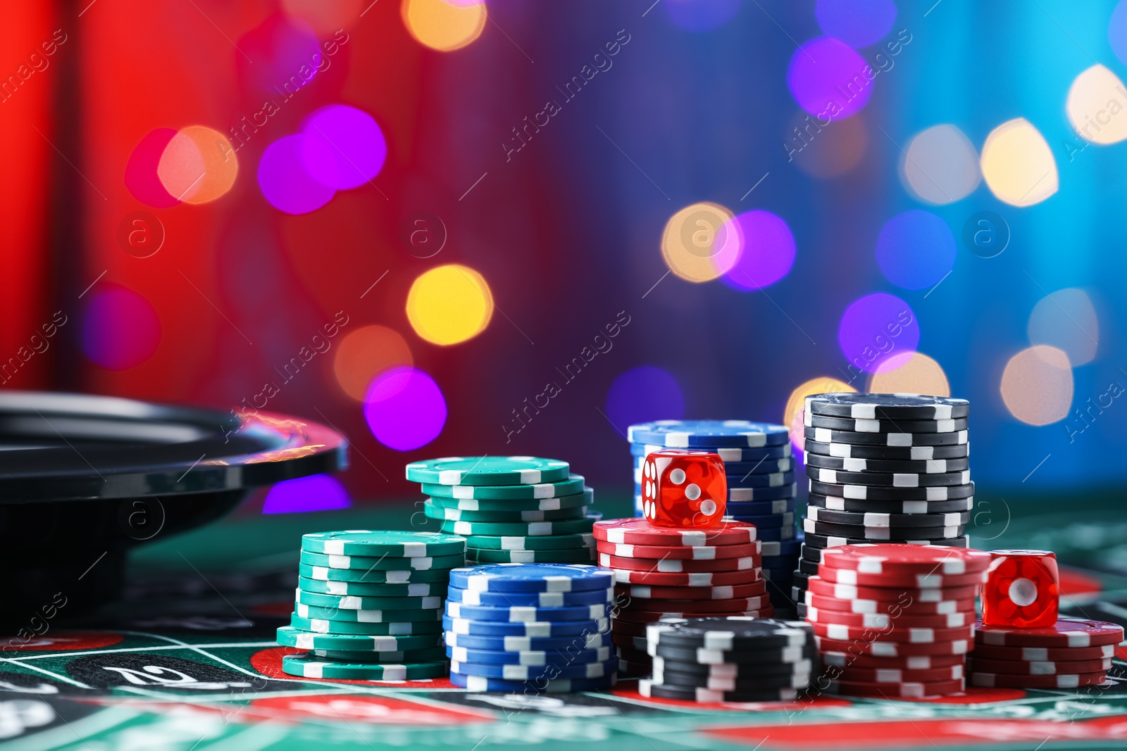 Photo of Casino chips and dice on roulette table against blurred lights, closeup