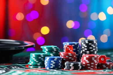 Photo of Casino chips and dice on roulette table against blurred lights, closeup