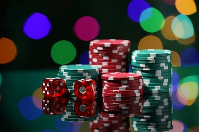 Photo of Casino chips and dice on mirror surface against blurred lights, closeup