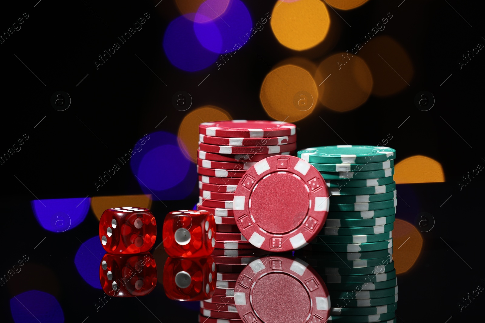 Photo of Casino chips and dice on mirror surface against blurred lights, closeup