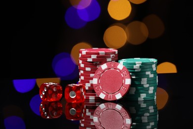 Photo of Casino chips and dice on mirror surface against blurred lights, closeup