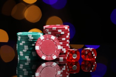Photo of Casino chips and dice on mirror surface against blurred lights, closeup