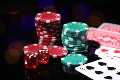 Photo of Casino chips, playing cards and dice on mirror surface against blurred lights, closeup