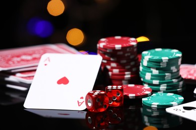 Photo of Casino chips, playing cards and dice on mirror surface against blurred lights, closeup