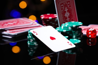 Photo of Casino chips, playing card and die on mirror surface against blurred lights, closeup