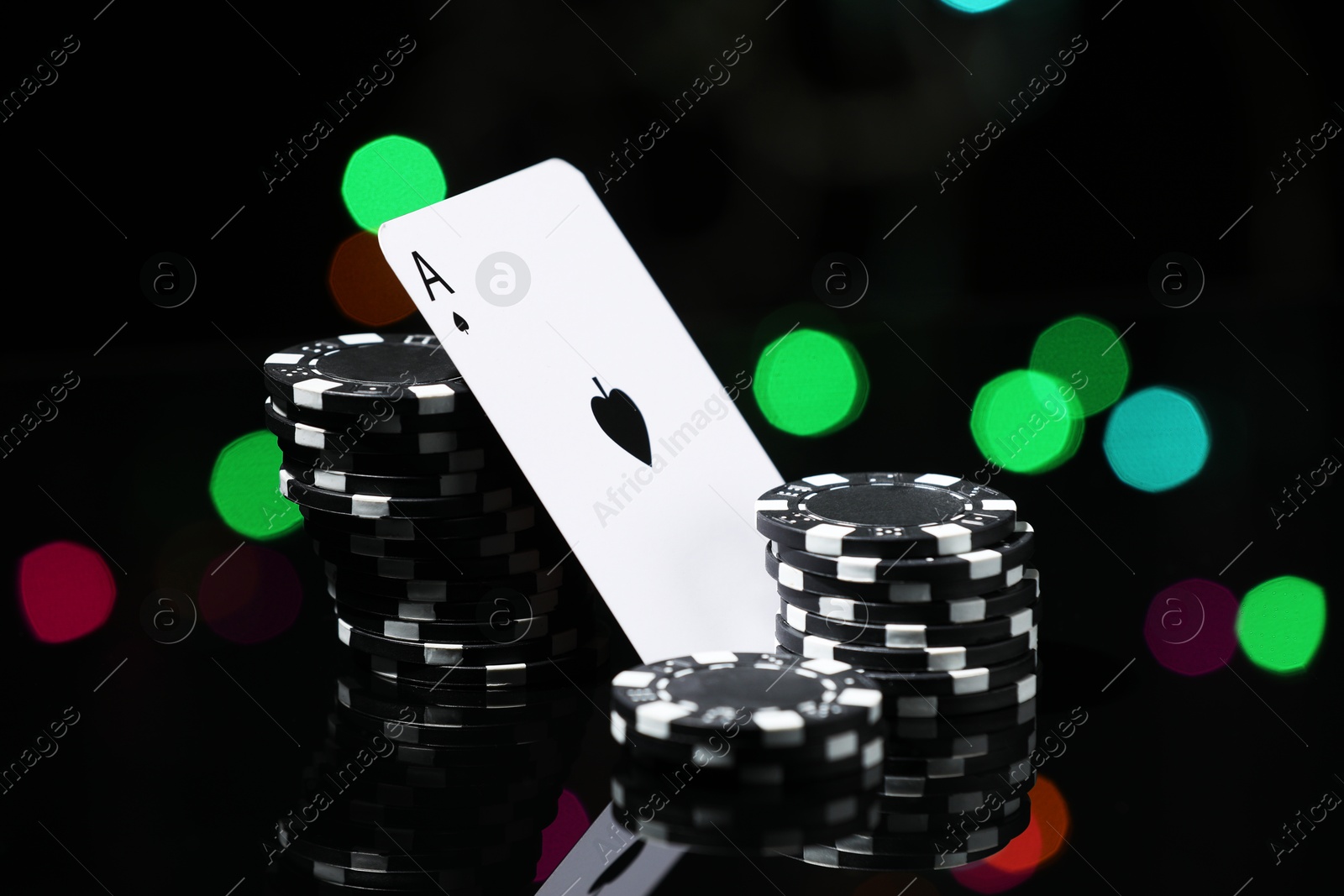 Photo of Casino chips and playing card on mirror surface against blurred lights, closeup