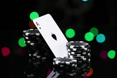 Photo of Casino chips and playing card on mirror surface against blurred lights, closeup