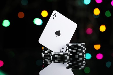 Photo of Casino chips and playing card on mirror surface against blurred lights, closeup