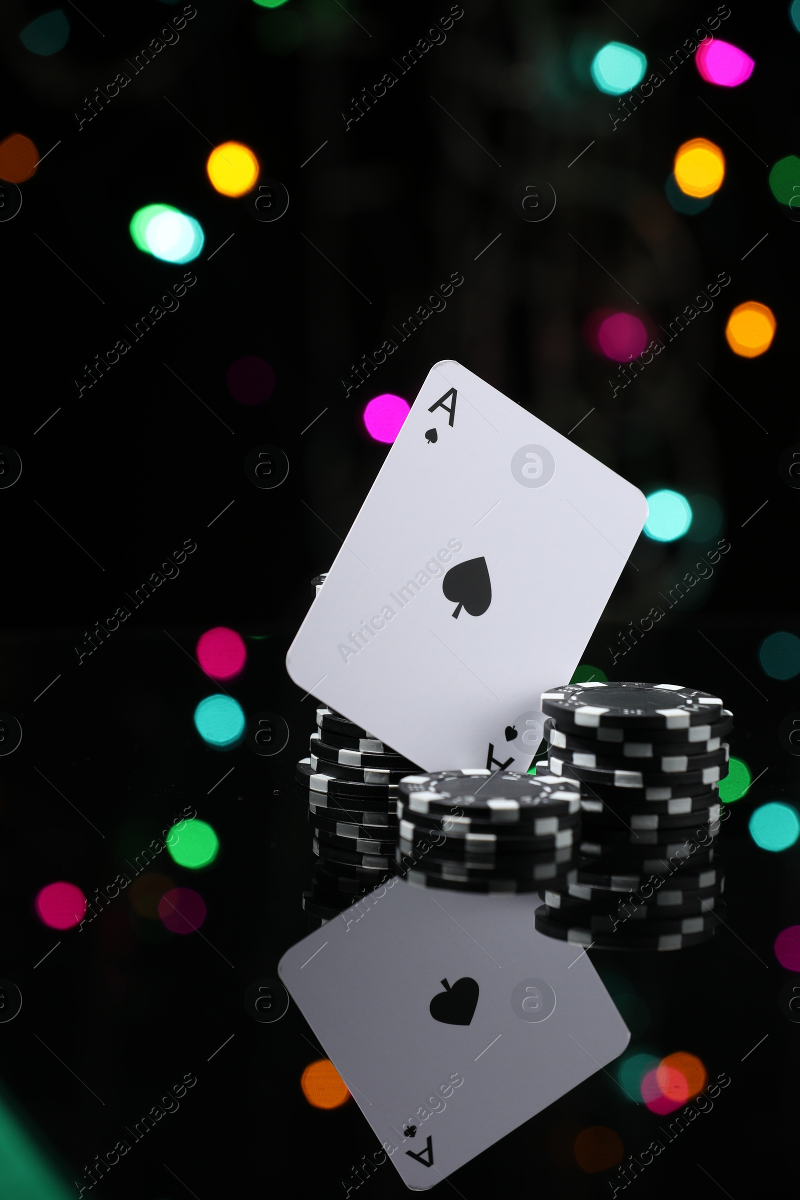 Photo of Casino chips and playing card on mirror surface against blurred lights, closeup