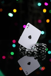 Photo of Casino chips and playing card on mirror surface against blurred lights, closeup