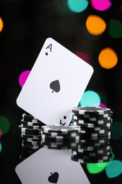 Photo of Casino chips and playing card on mirror surface against blurred lights, closeup