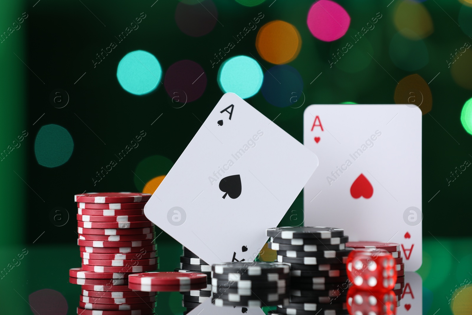 Photo of Casino chips, playing cards and dice on mirror surface against blurred lights, closeup