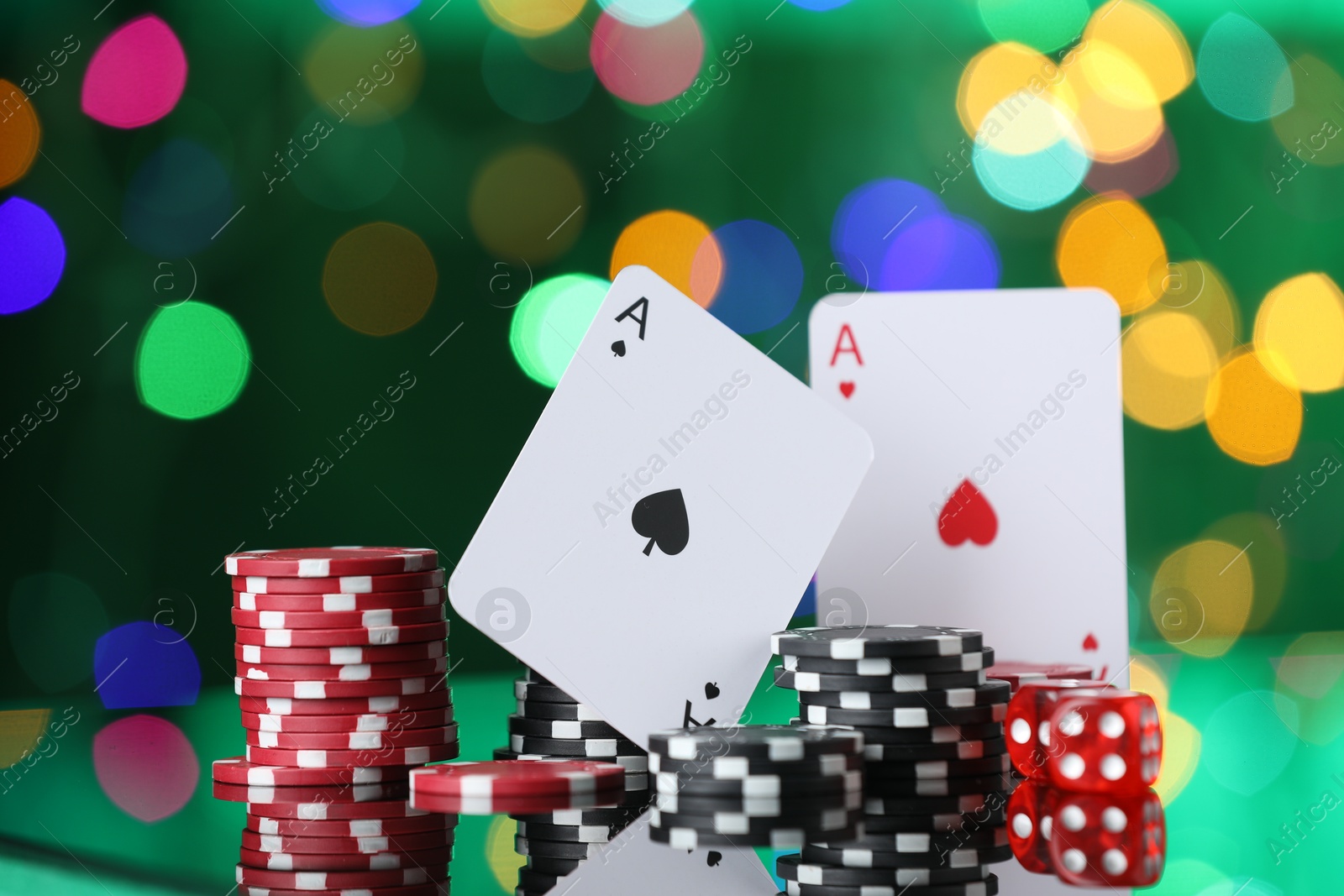Casino chips, playing cards and dice on mirror surface against blurred lights, closeup Photo of Casino chips, playing cards and dice on mirror surface against blurred lights, closeup