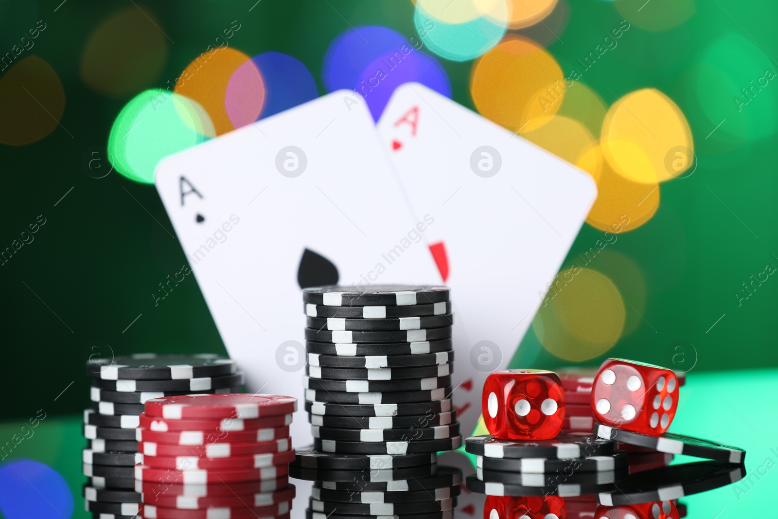 Casino chips, playing cards and dice on mirror surface against blurred lights, closeup Photo of Casino chips, playing cards and dice on mirror surface against blurred lights, closeup