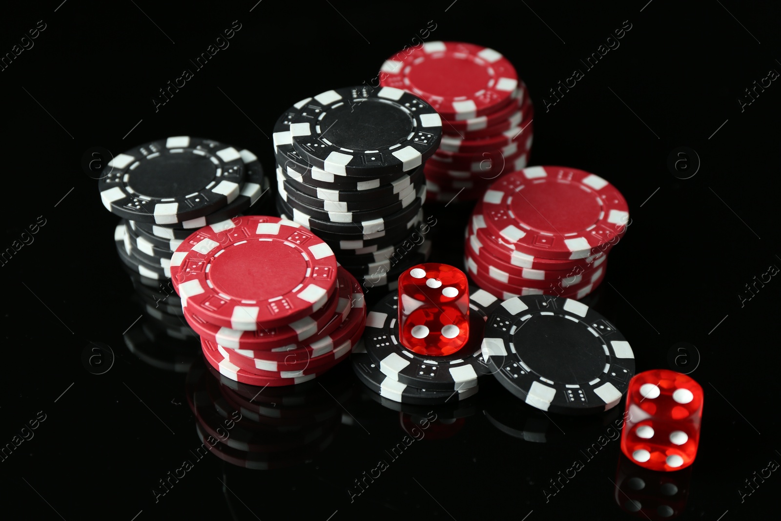 Photo of Casino chips and dice on mirror surface against black background, closeup
