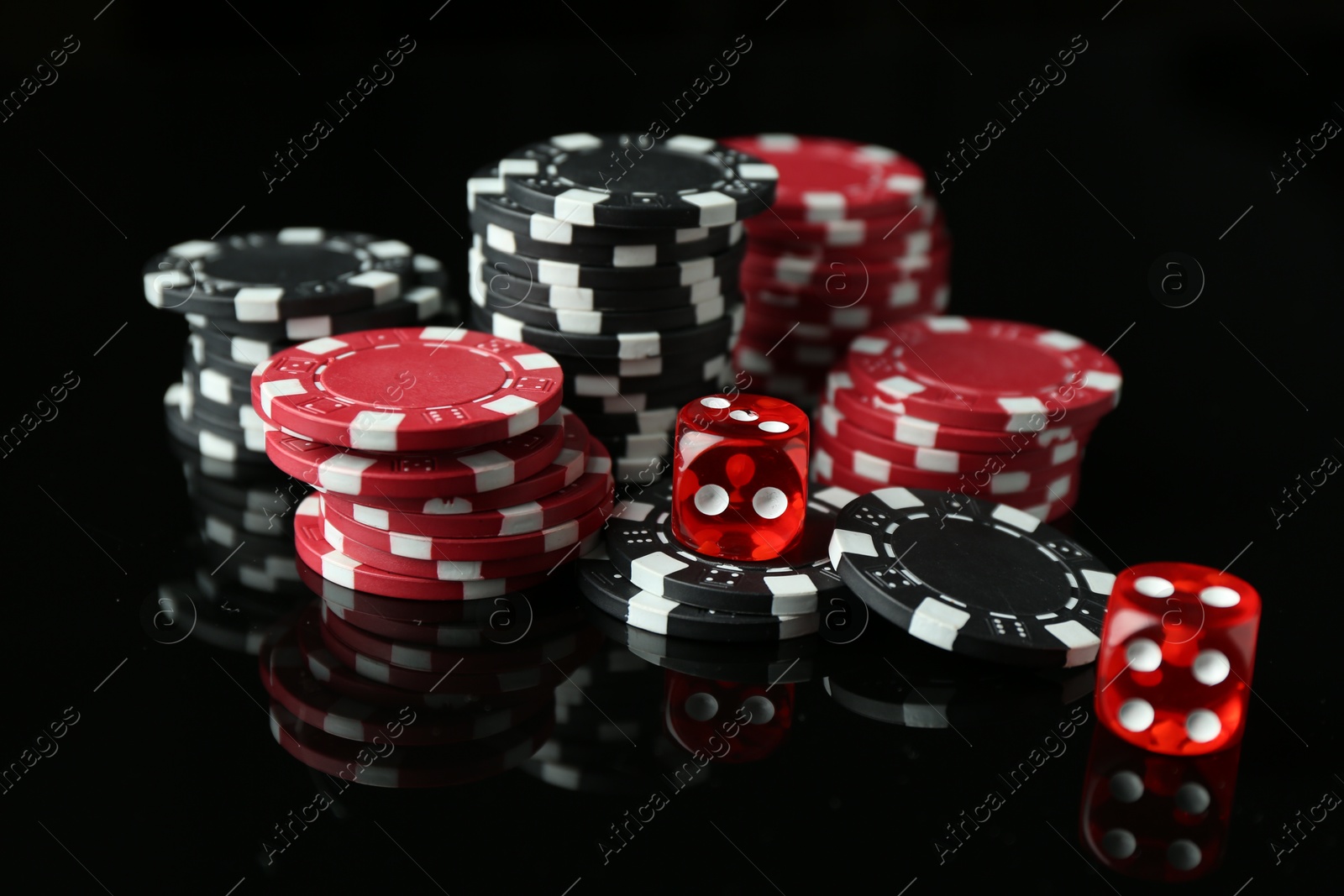 Photo of Casino chips and dice on mirror surface against black background, closeup