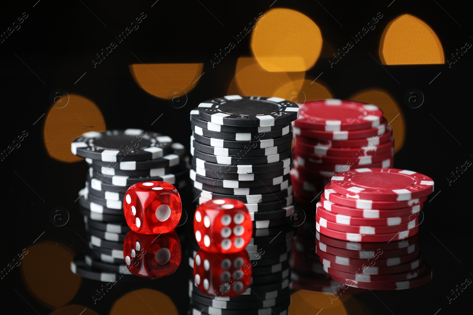 Photo of Casino chips and dice on mirror surface against blurred lights, closeup