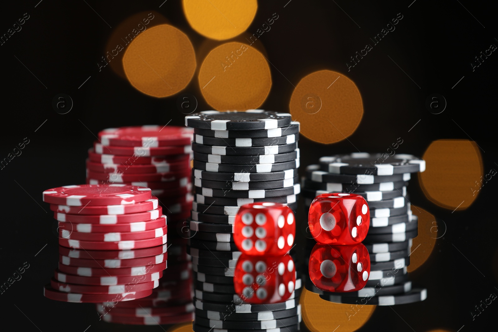 Photo of Casino chips and dice on mirror surface against blurred lights, closeup