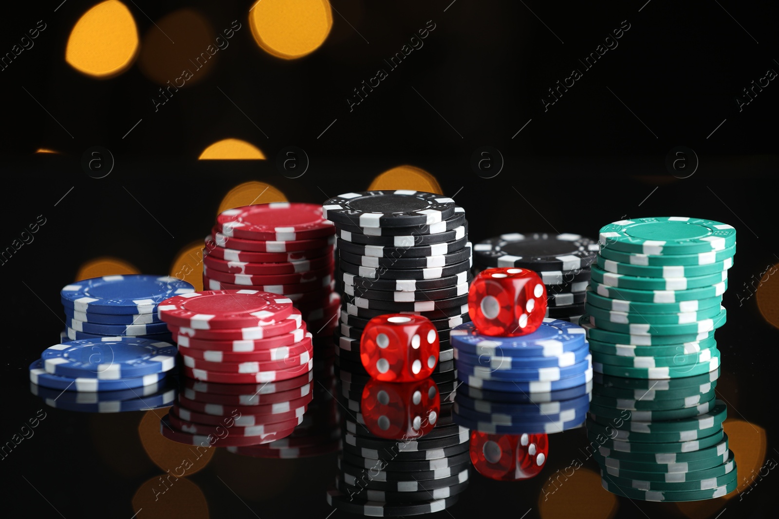 Photo of Casino chips and dice on mirror surface against blurred lights, closeup