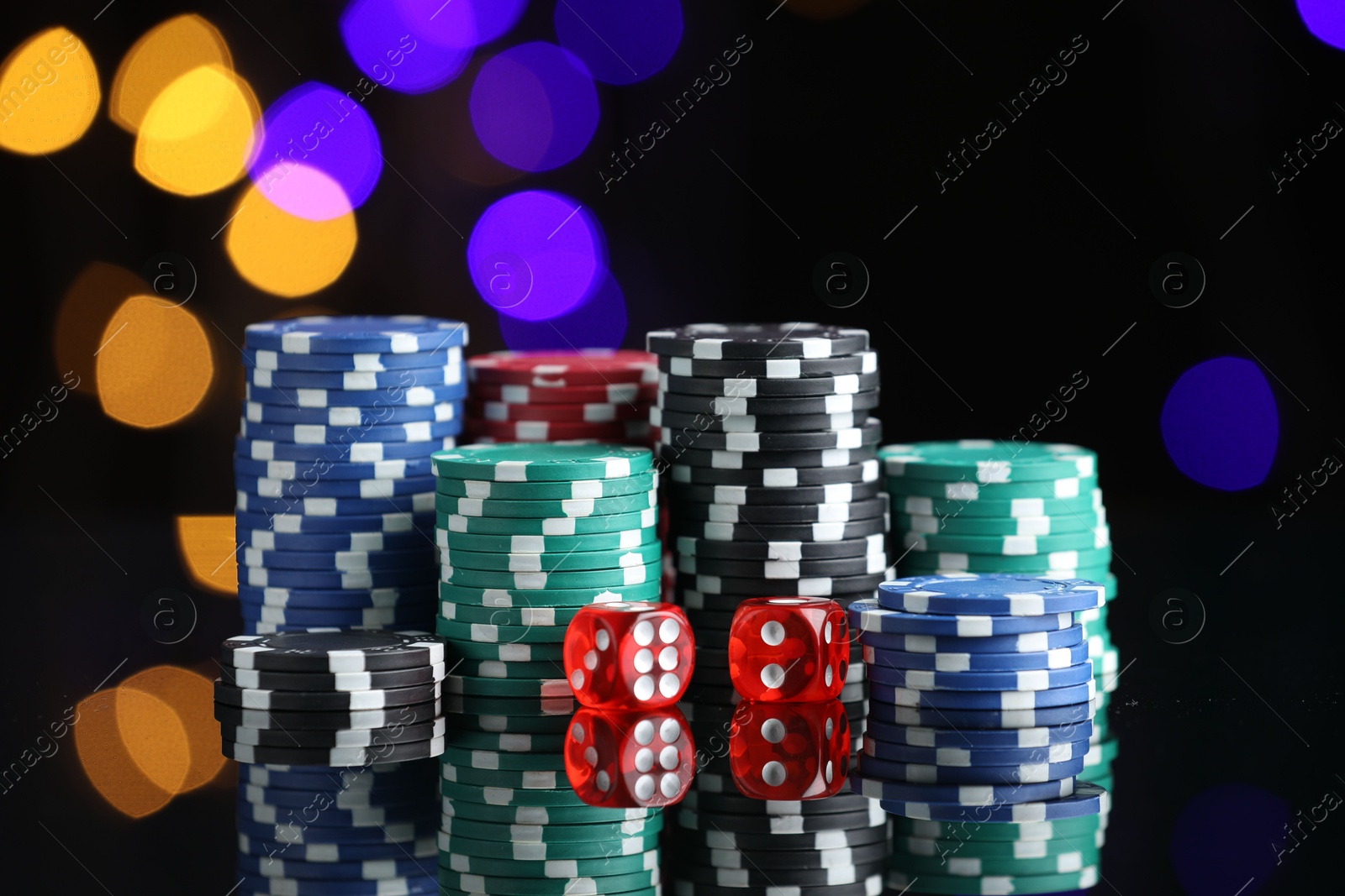 Photo of Casino chips and dice on mirror surface against blurred lights, closeup