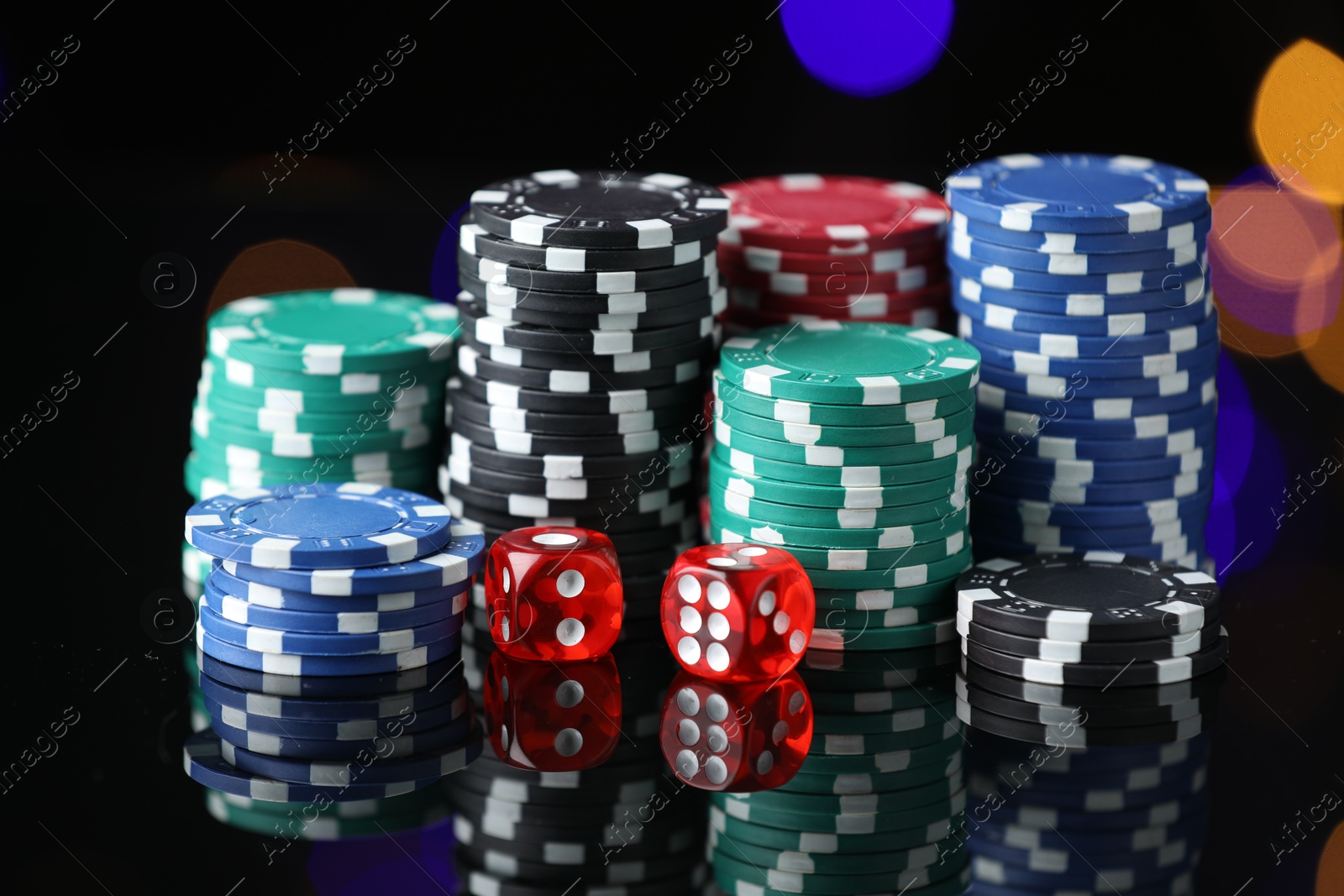 Photo of Casino chips and dice on mirror surface against blurred lights, closeup