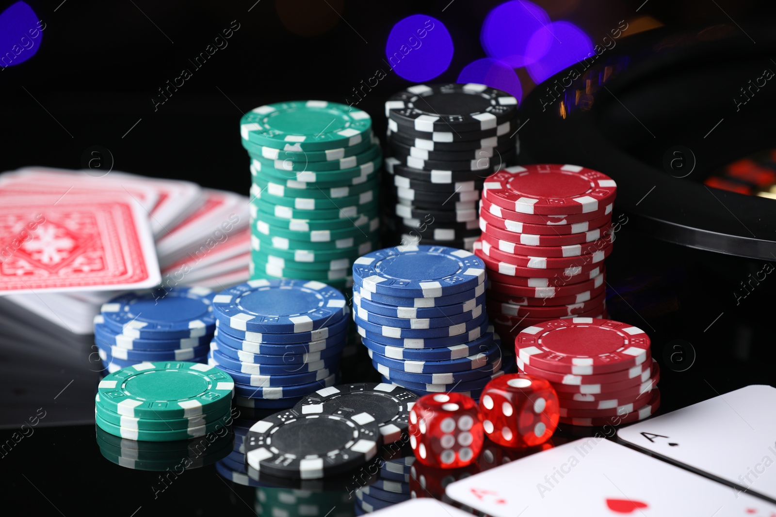 Photo of Casino chips, playing cards and dice on mirror surface against blurred lights, closeup