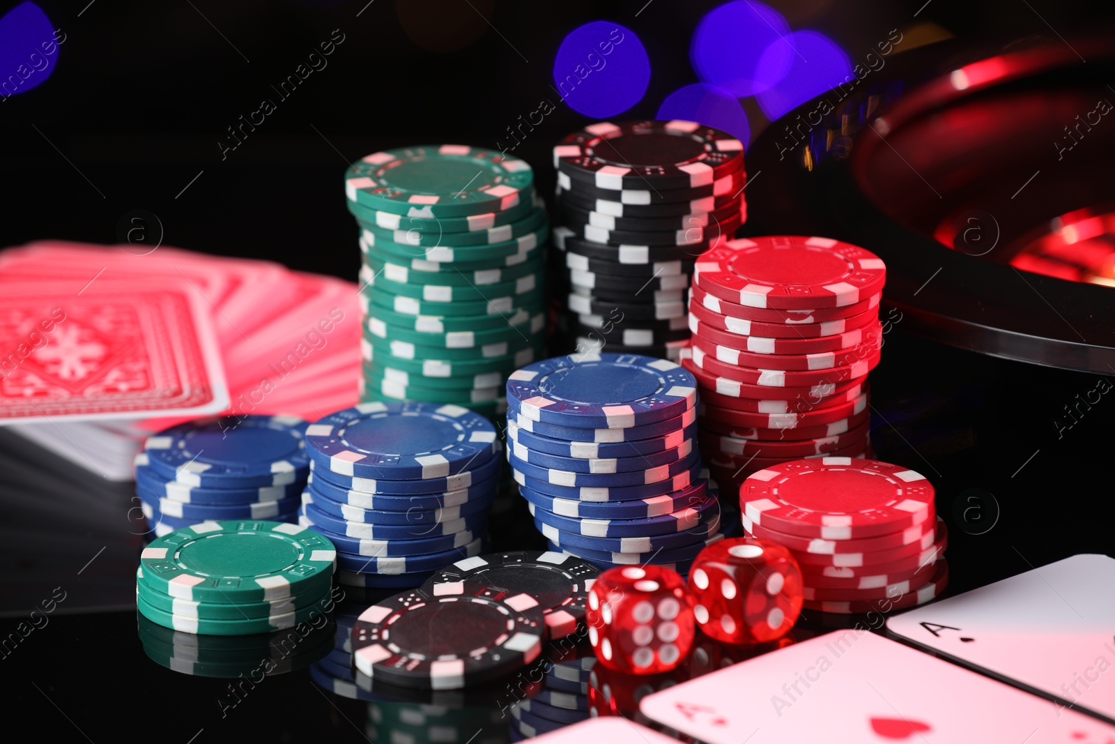 Photo of Casino chips, playing cards and dice on mirror surface against blurred lights, closeup