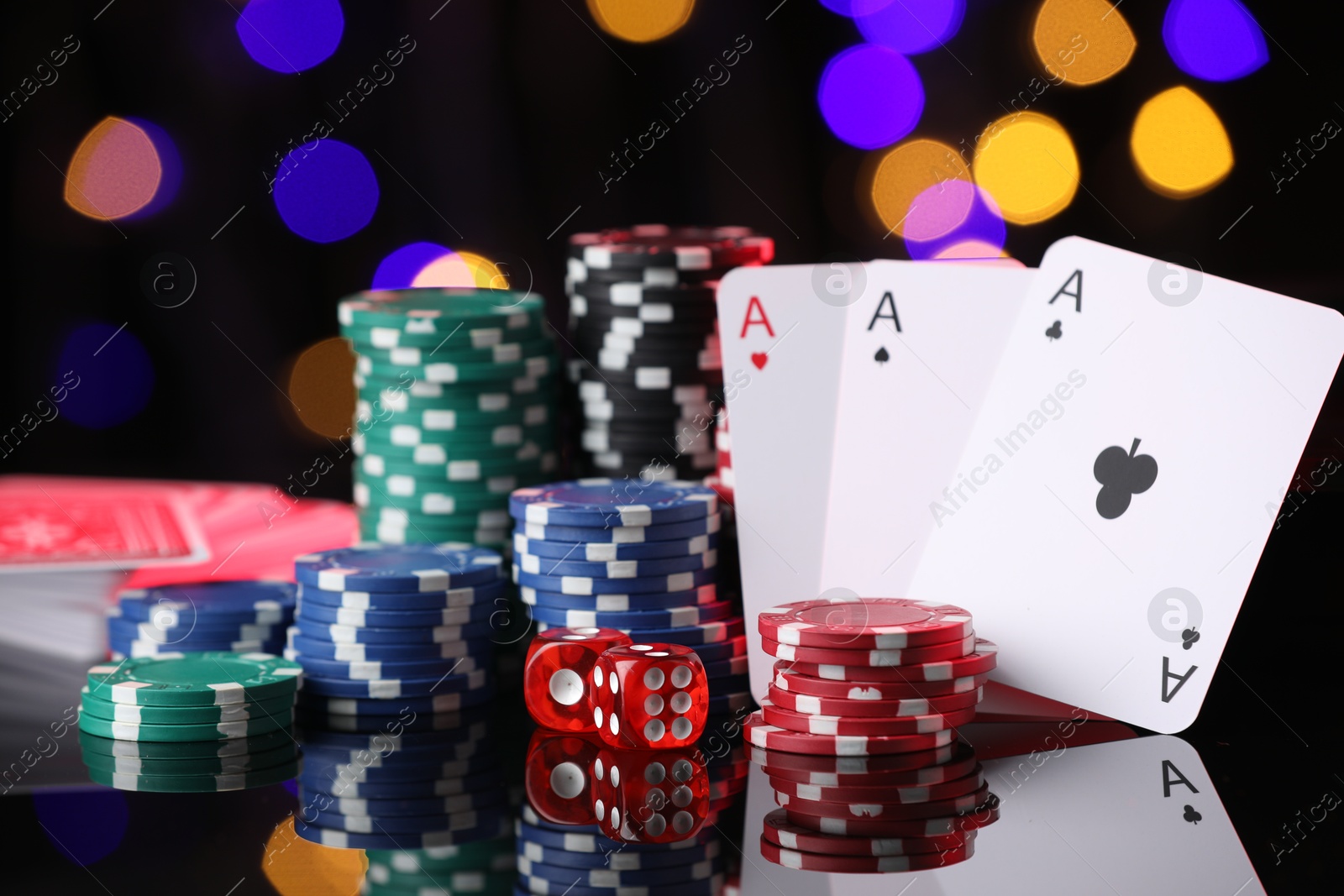 Casino chips, playing cards and dice on mirror surface against blurred lights, closeup Photo of Casino chips, playing cards and dice on mirror surface against blurred lights, closeup