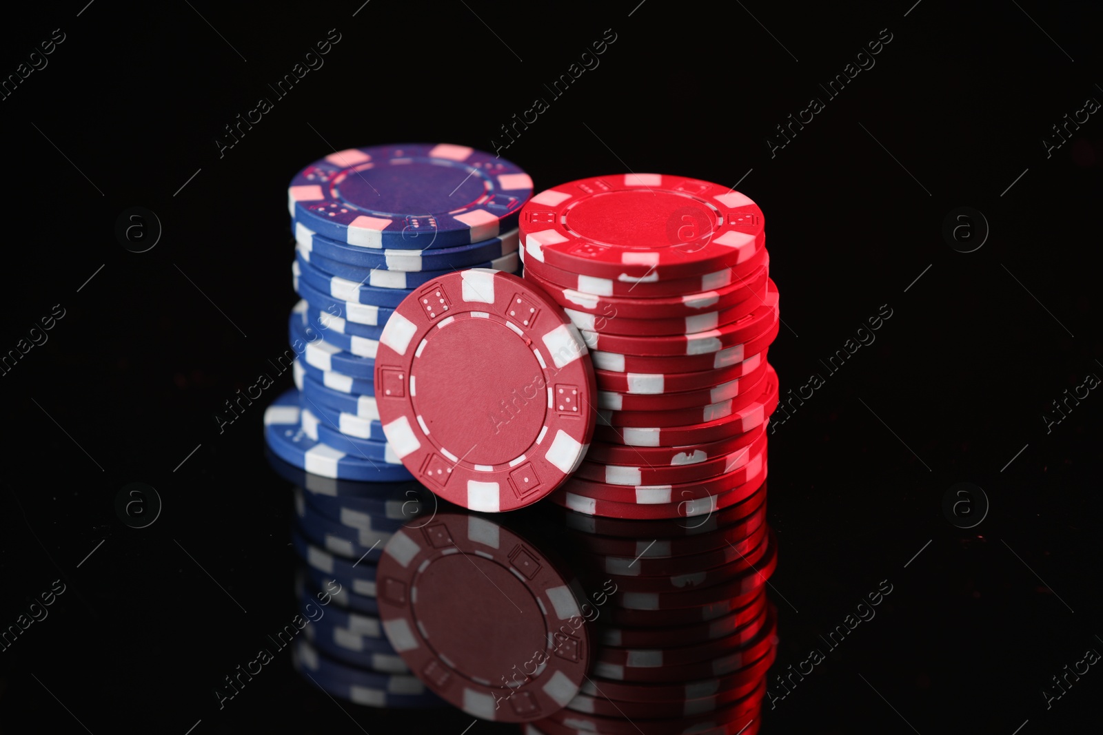 Photo of Casino chips on mirror surface against black background, closeup