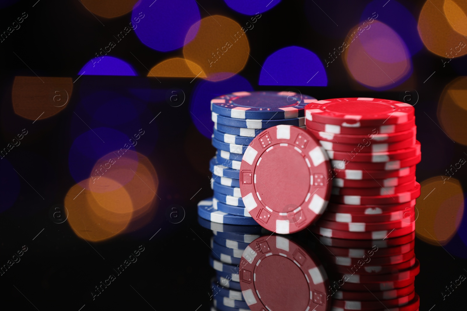 Casino chips on mirror surface against blurred lights, closeup. Space for text Photo of Casino chips on mirror surface against blurred lights, closeup. Space for text