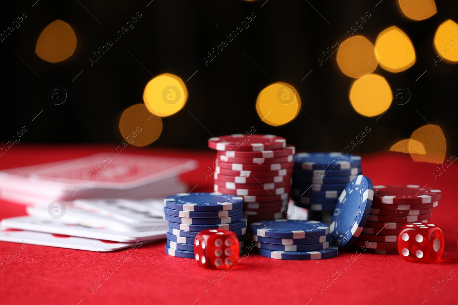Photo of Casino chips, playing cards and dice on red table against blurred lights, closeup