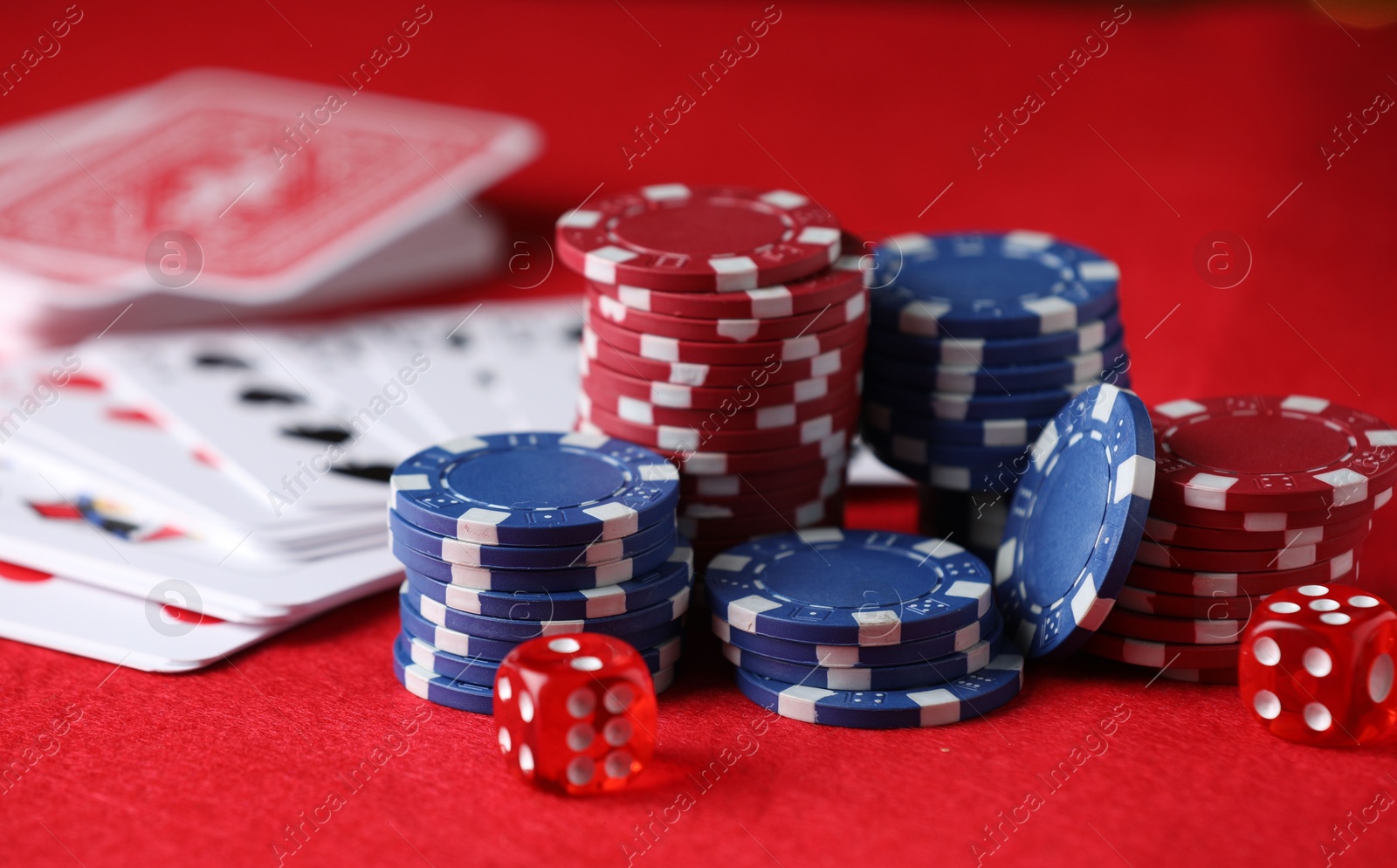 Photo of Casino chips, playing cards and dice on red table, closeup