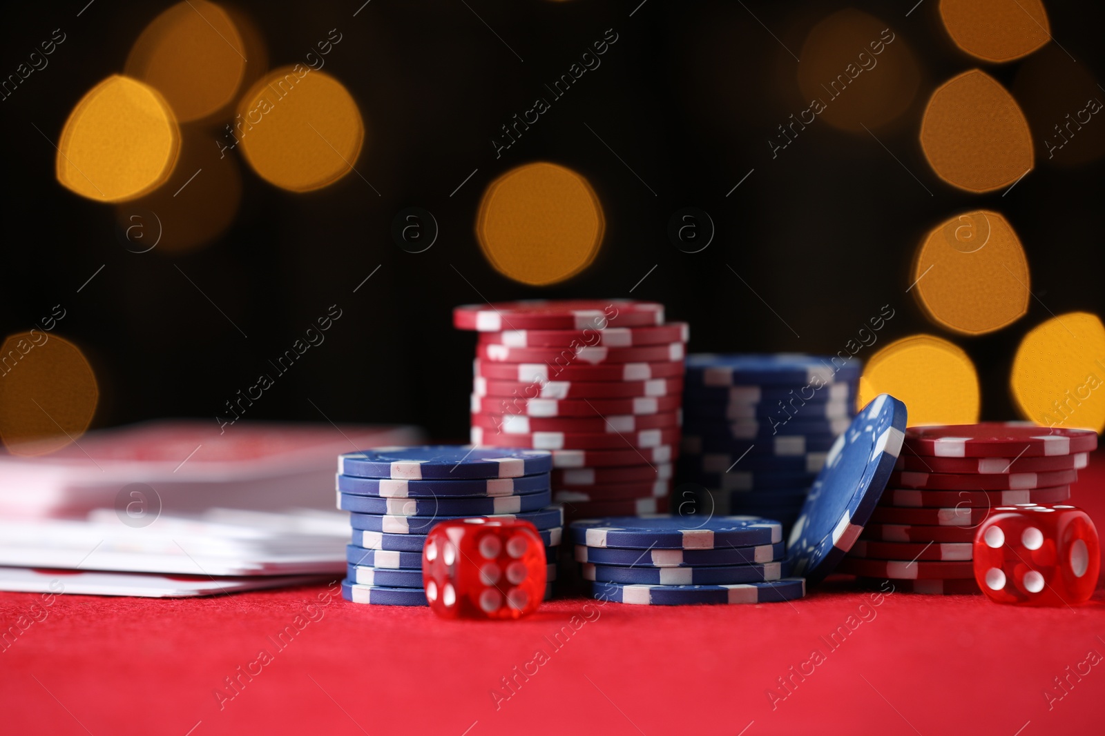 Photo of Casino chips, playing cards and dice on red table against blurred lights, closeup