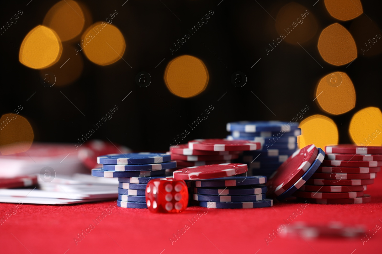 Casino chips, playing cards and die on red table against blurred lights, closeup Photo of Casino chips, playing cards and die on red table against blurred lights, closeup