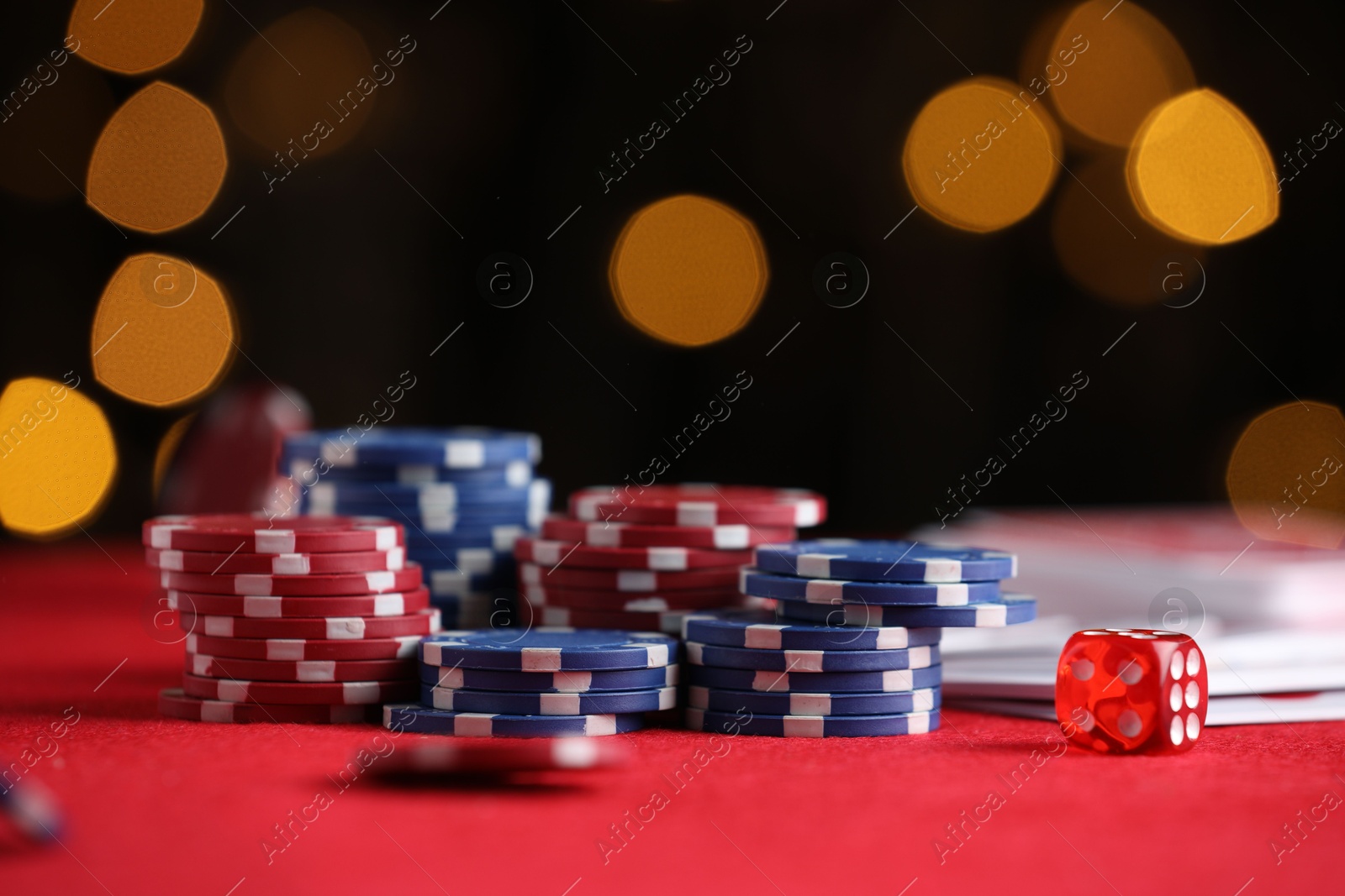 Casino chips, playing cards and die on red table against blurred lights, closeup Photo of Casino chips, playing cards and die on red table against blurred lights, closeup