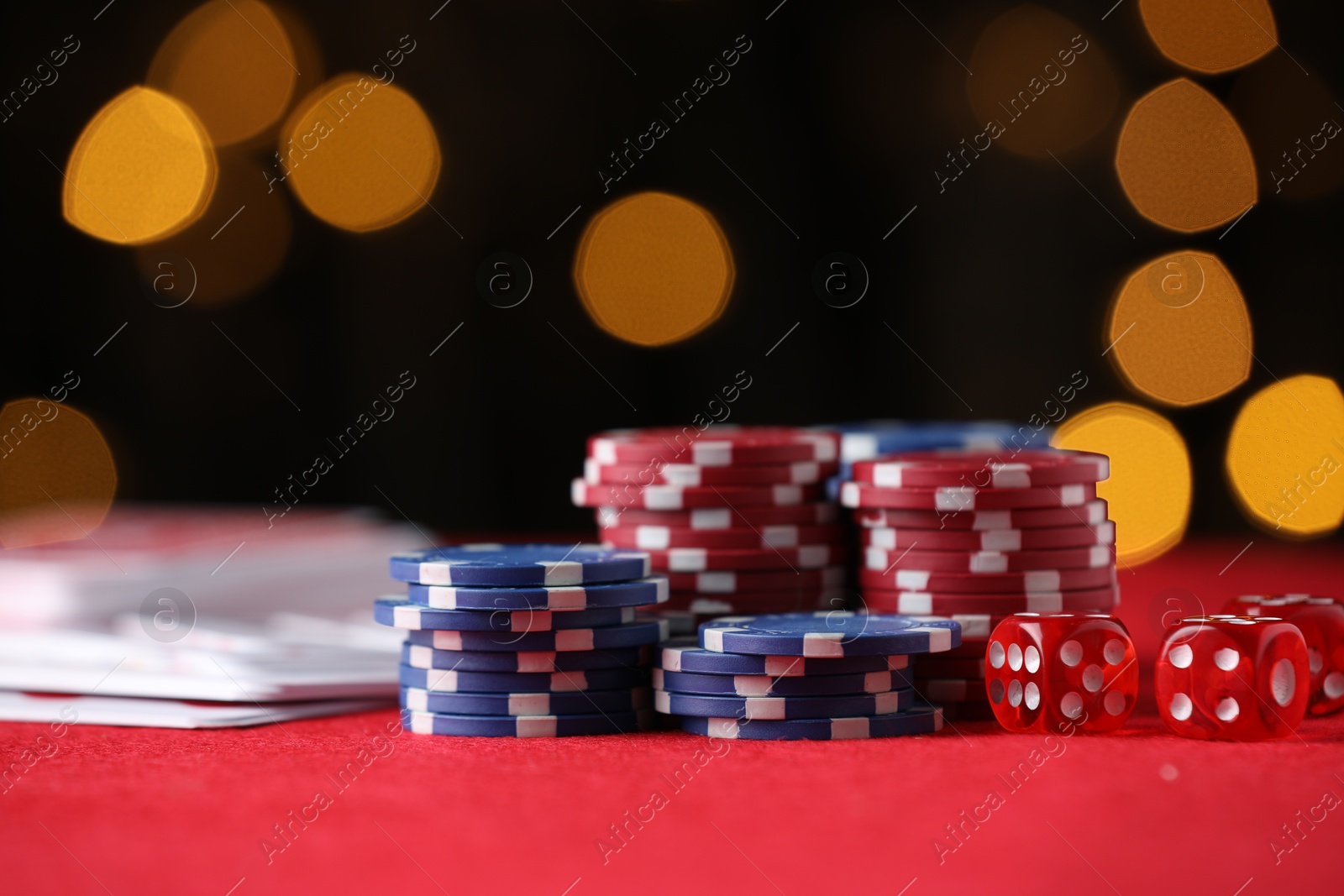 Photo of Casino chips, playing cards and dice on red table against blurred lights, closeup