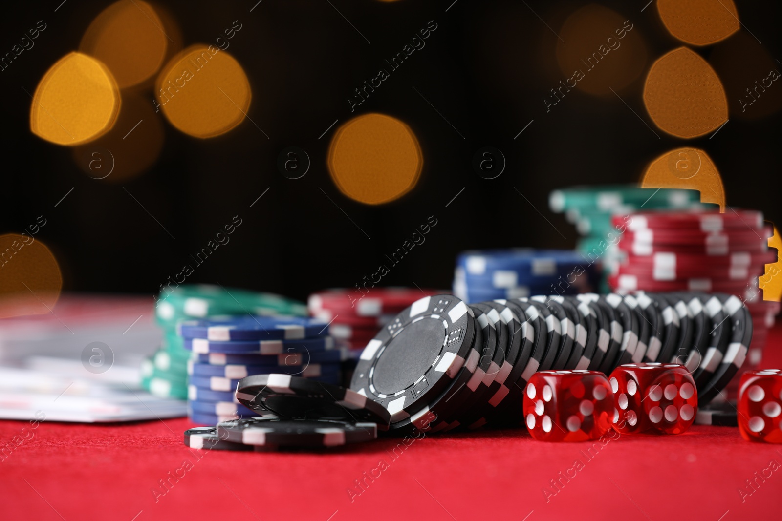 Photo of Casino chips, playing cards and dice on red table against blurred lights, closeup