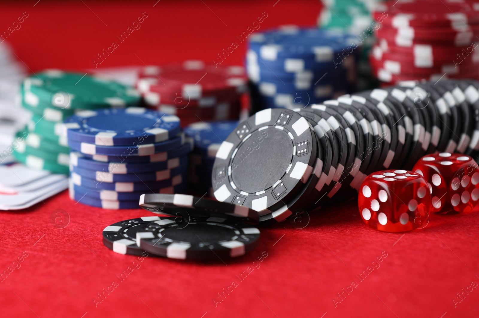 Photo of Casino chips, playing cards and dice on red table, closeup
