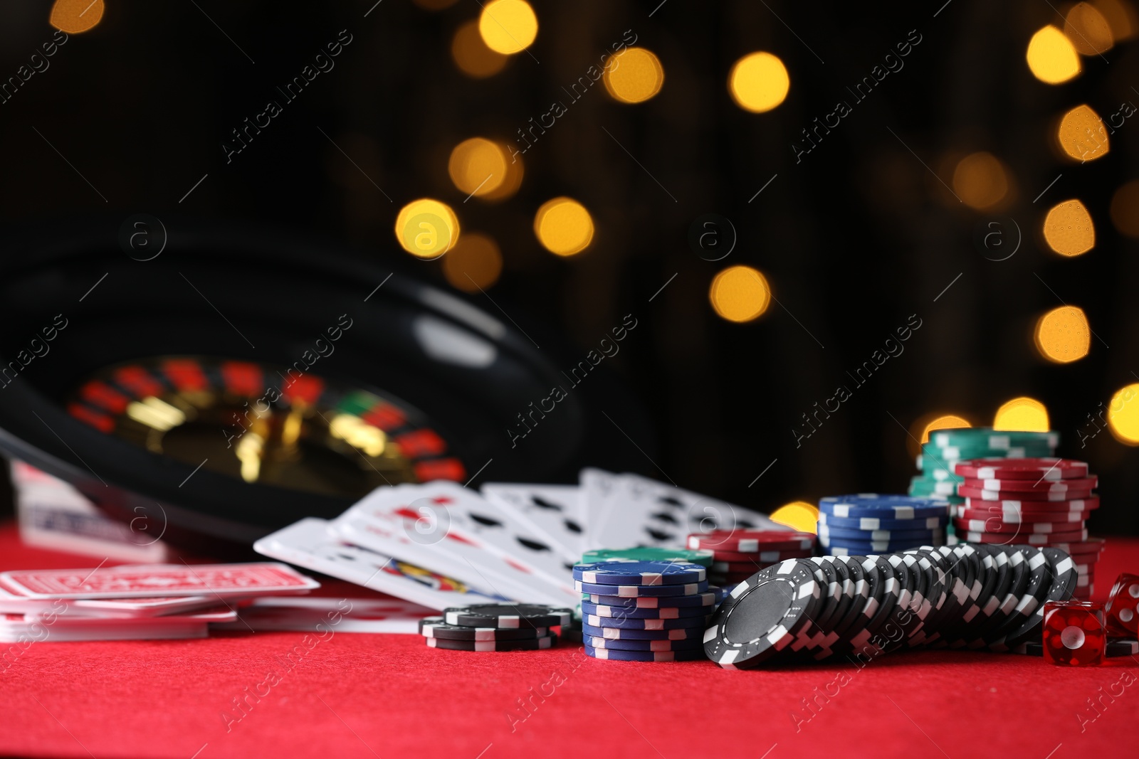 Photo of Casino chips, playing cards and dice on red table against blurred lights, closeup