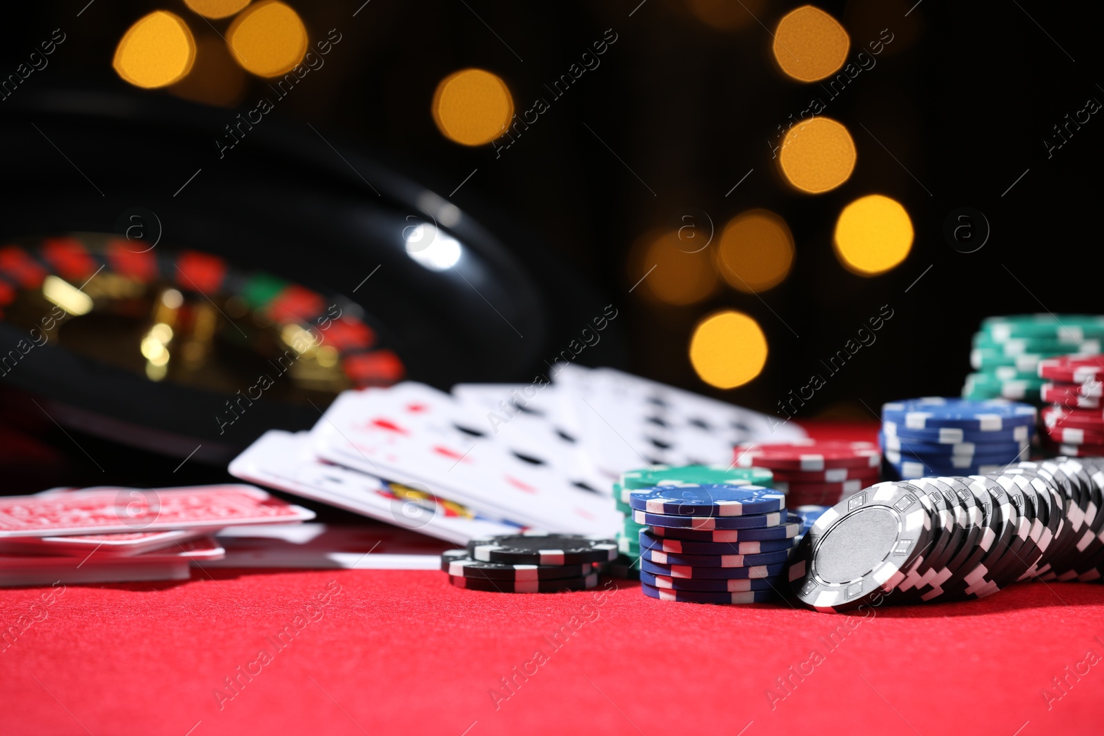 Casino chips and playing cards on red table against blurred lights, closeup Photo of Casino chips and playing cards on red table against blurred lights, closeup