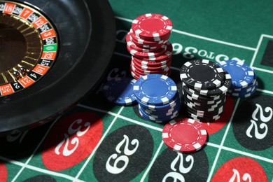 Photo of Casino chips and roulette wheel on table, closeup