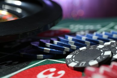 Photo of Casino chips and roulette wheel on table against blurred lights, closeup