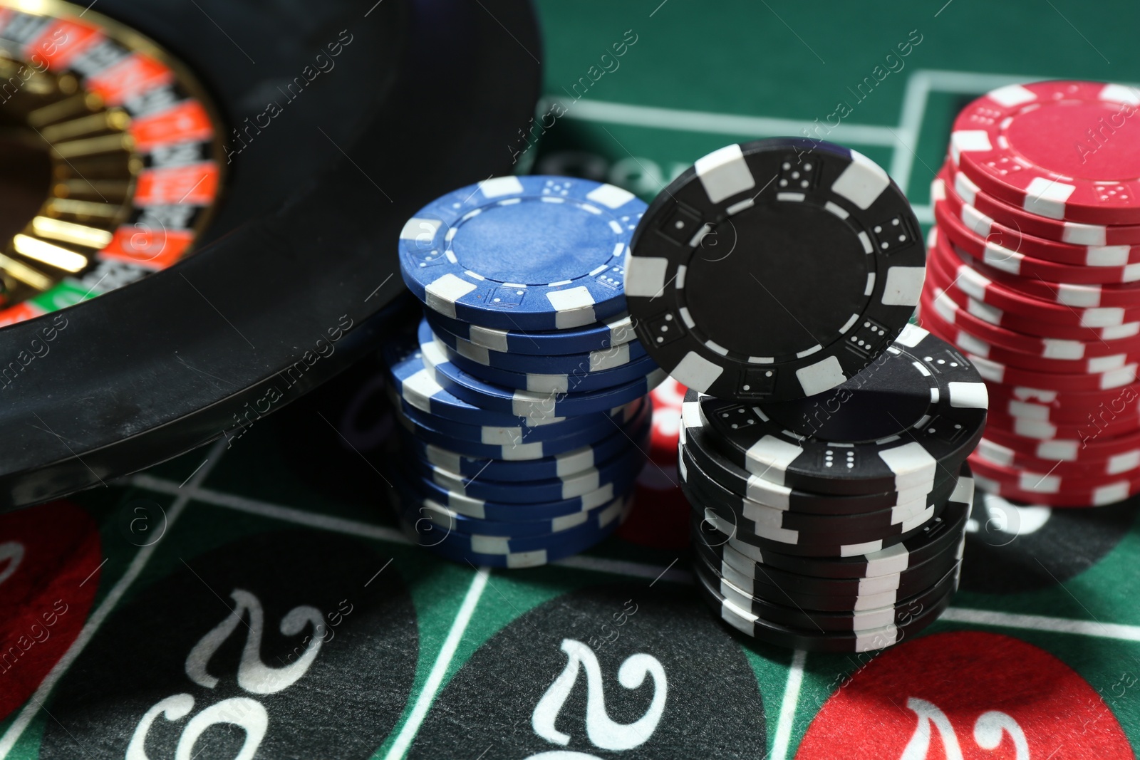 Photo of Casino chips and roulette wheel on table, closeup