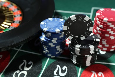 Photo of Casino chips and roulette wheel on table, closeup