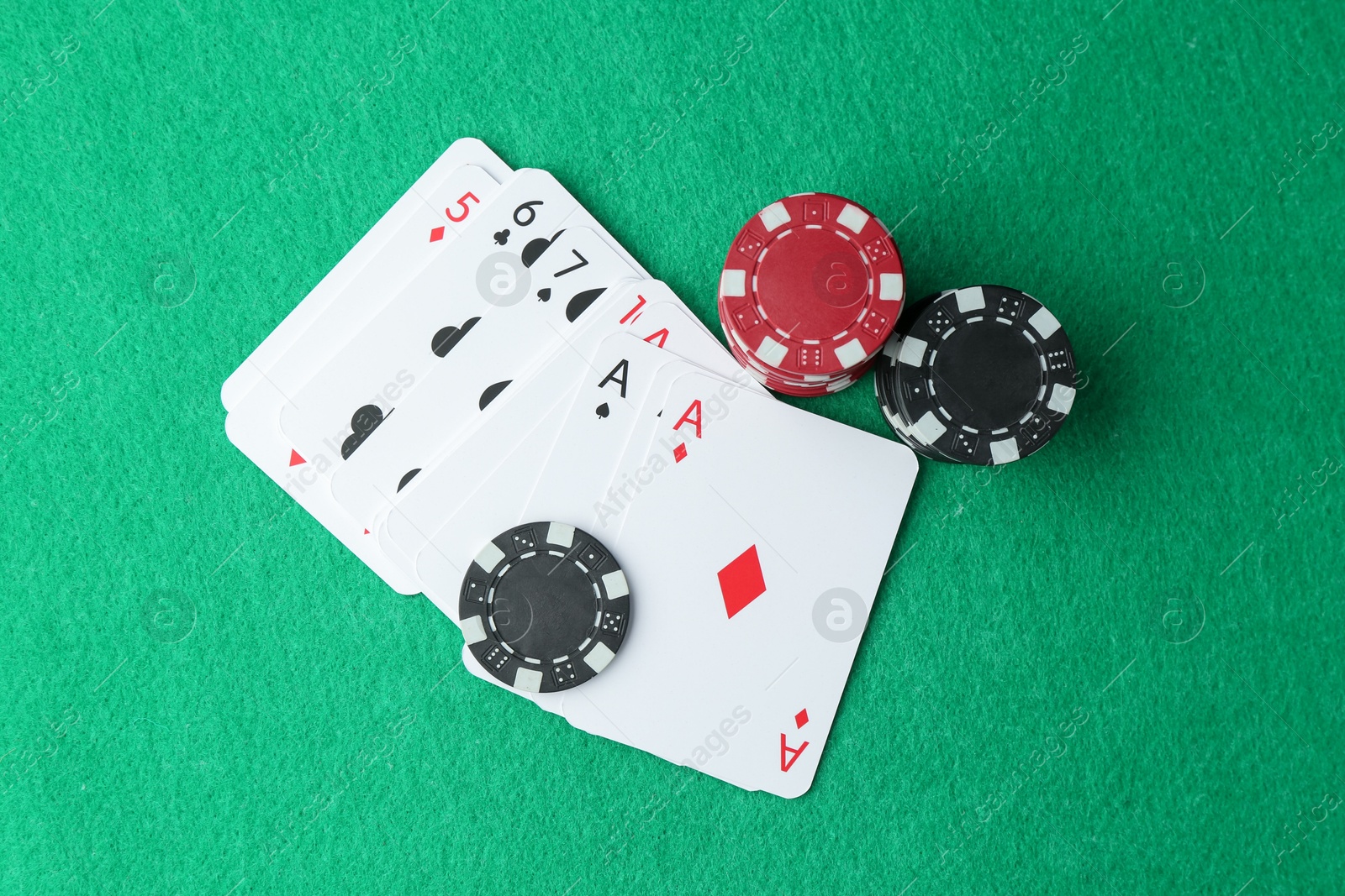 Photo of Casino chips and playing cards on green table, flat lay