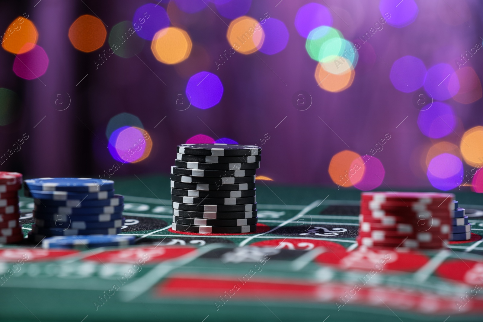 Casino chips on roulette table against blurred lights, closeup Photo of Casino chips on roulette table against blurred lights, closeup