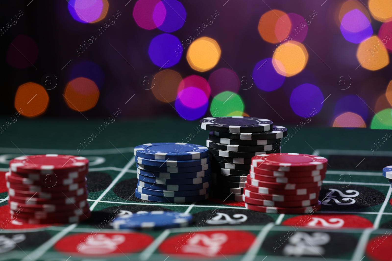 Photo of Casino chips on roulette table against blurred lights, closeup