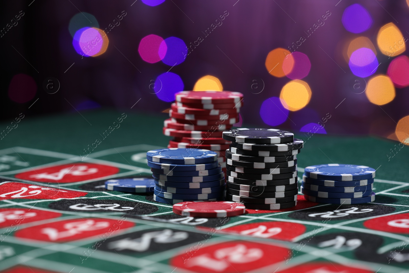 Casino chips on roulette table against blurred lights, closeup Photo of Casino chips on roulette table against blurred lights, closeup