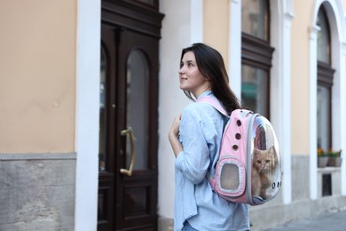 Photo of Woman with her cute cat in backpack carrier on city street. Space for text